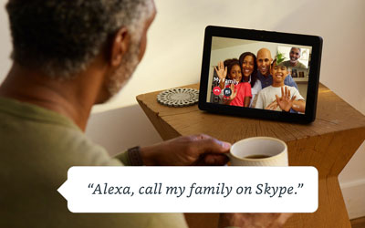  An Echo Show on a desk with screen showing interface of video chat. In front of it is a male holding a cup of coffee. At the lower part of the picture is a dialog box containing texts reading as “Alexa, call my family on Skype.”  